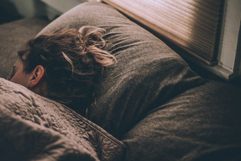 Iemand slaapt diep onder een wit dekbed in een donkere slaapkamer