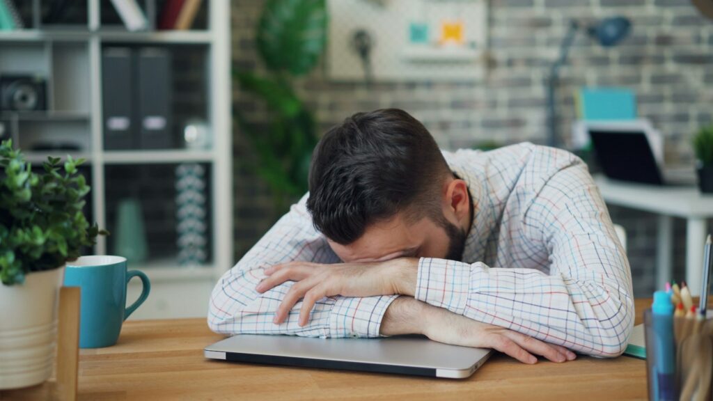 Tiener slaapt met het hoofd op een stapel schoolboeken aan een bureau