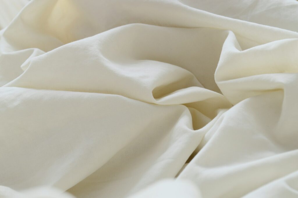 Opgemaakt bed met een dik wit dekbed in een lichte slaapkamer