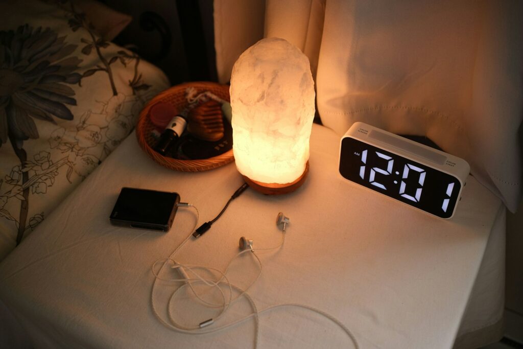 Nachtkastje naast een opgemaakt bed met een telefoon en een lamp